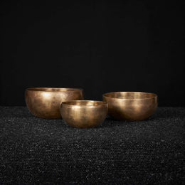 Three brass bowls on a dark textured surface with a black background